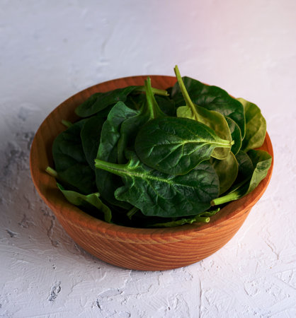 green spinach leaves in a brown wooden bowl on a white surface, close upの写真素材