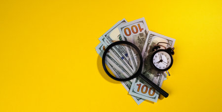 paper american hundred dollar bills and a magnifying glass on a yellow background. The concept of search for earnings, profit with less time, reward. Baner, copy spaceの写真素材