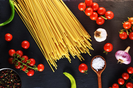 Uncooked pasta spaghetti on black background, red cherry tomatoes and garlic for sauce, top viewの写真素材