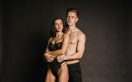 woman in black lingerie and shirtless man standing and hugging on black backgroundの素材