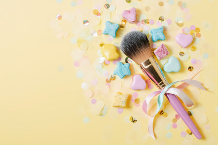Makeup brush with bright sweets and confetti on a yellow backgroundの素材