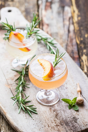 Peach and rosemary fizz cocktail on a wooden background.の素材