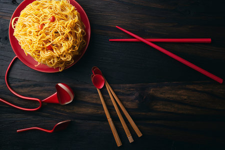 Yellow instant noodle on black wood background has red chopsticks wolfberryの素材