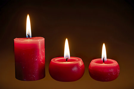 A photo of three red candles with distinct flame sizes against a pitch-black backgroundの写真素材