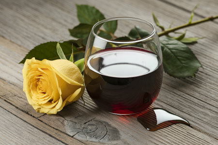 A photo of a red wine glass and a yellow roseの写真素材