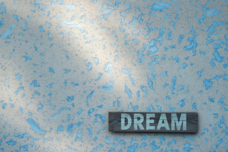 A rustic wooden sign with the word DREAM is mounted on a light blue textured wall. Sunlight casts a shadow across the wall.の写真素材