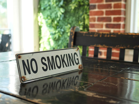 A weathered 'No Smoking' sign rests on a dark, glossy wooden table. In the background, a lush green wall and a brick wall create a textured, inviting atmosphere.の写真素材