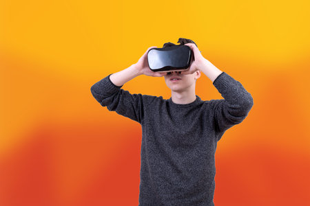 The man with glasses of virtual reality on colored background. Young guy in VR headset is looking at interactive screen. Playing mobile game app on device.の写真素材