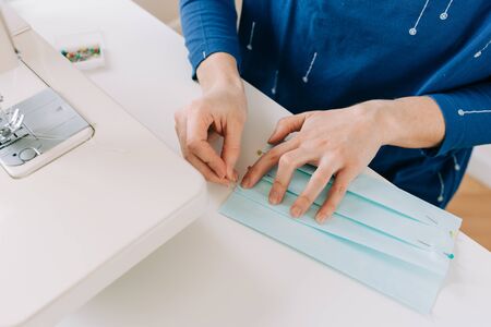 Woman hands using the sewing machine to sew the face home made diy medical mask during the coronavirus pandemia.の写真素材