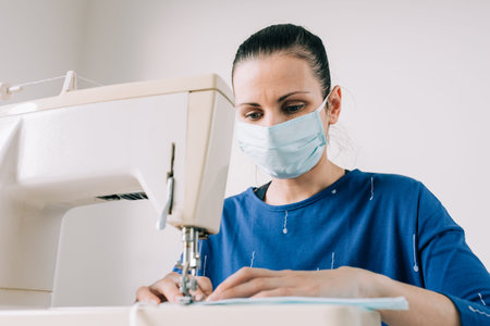 Woman hands using the sewing machine to sew the face home made diy medical mask during the...
