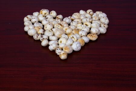 Makhana also know as lotus seeds are arranged or grouped in heart shape on brown wooden table shows health benefit towards heartの写真素材
