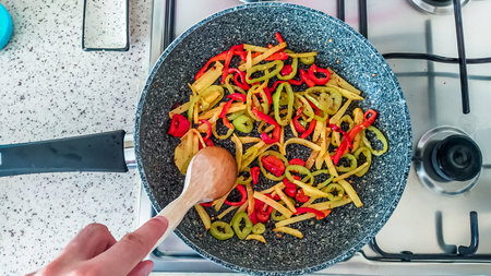 Top view of cooking vegetables with peppers and potatoes in a frying pan, representing home cooking.の写真素材