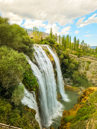 Tortum Selalesi or Tortum Waterfall cascades under blue skies and lush greenery, evoking nature's power and tranquilityの写真素材