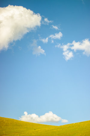 Serene green hill under a bright blue sky with a lone cloud, symbolizing simplicity and clarity vertical backgroundの写真素材