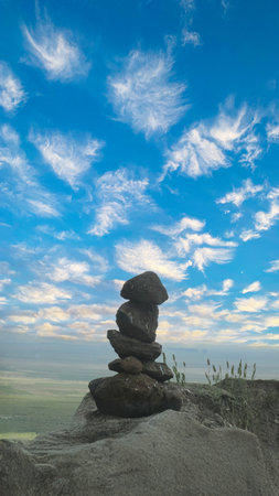 A tranquil scene of stacked stones against a vibrant blue sky, symbolizing harmony, balance, and tranquility in nature. A perfect minimalist wallpaper for meditation.の写真素材