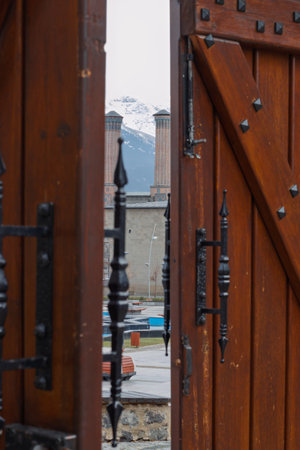 Framed by a decorative wooden gate, Erzurum iconic Twin Minaret Madrasa or Cifte Minareli Medrese stands against a backdrop of snowy mountainsの写真素材