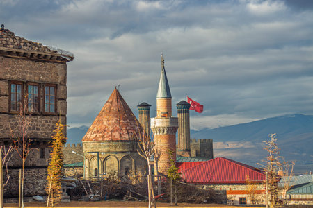 An iconic view of the Twin Minaret Madrasa, Erzurum's historic stone house, and tiled minaret,...