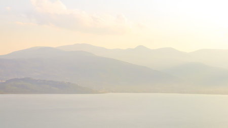 A serene scene featuring hazy mountain layers and a calm lake, evoking peace, quiet, and minimalism under soft light.の写真素材