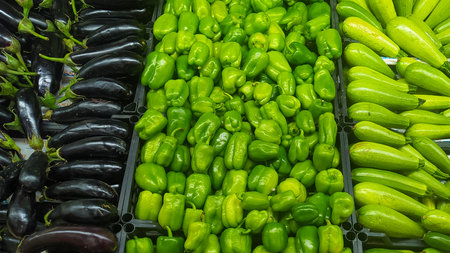 Colorful arrangement of fresh eggplants, green peppers, and zucchinis in a market, symbolizing food prices, shopping trends, and the concept of sustainabilityの写真素材