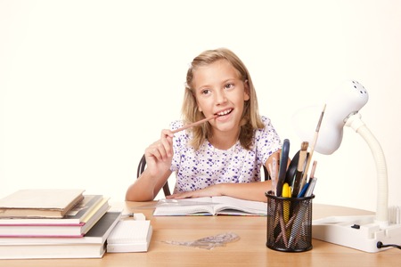 happy young school girl sitting at the table with a ruler and draw a line in the bookletの写真素材