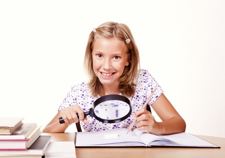 happy young school girl sit with a magnifying glass in hand and write homeworkの写真素材