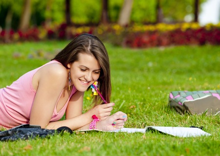 young high school student or college girl lying on the grass in the park and learnの写真素材
