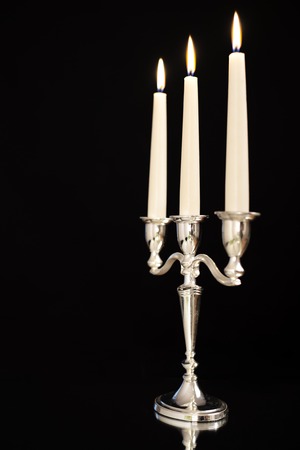 silver candlestick with three burning white candles in front of black backgroundの写真素材