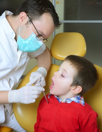 little boy in a red sweater went to the dentist in the dental chair sits next to a doctor to do the dentist to see if his teeth were okayの写真素材