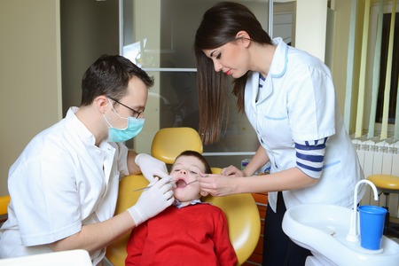 little boy in a red sweater went to the dentist in the dental chair sits next to a doctor to do the dentist to see if his teeth were okayの写真素材