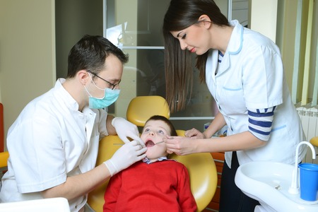 little boy in a red sweater went to the dentist in the dental chair sits next to a doctor to do the dentist to see if his teeth were okayの写真素材