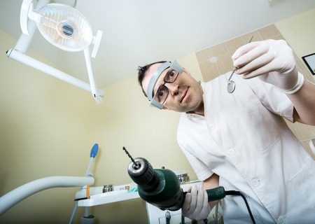 crazy dentist ready to drill approached the patient and dental instruments keeping the hands that protected surgical glovesの写真素材