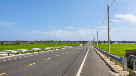 Asphalt road with green rice field and blue sky in Thailand.