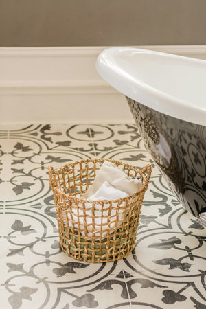 Bathtub and basket with towel on tile floor in bathroom.の写真素材