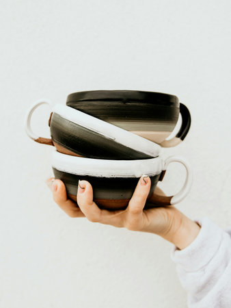 Female hand holding black and white ceramic cups against a white wallの写真素材