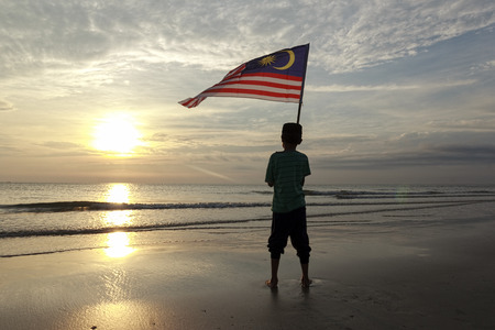 The Concept of Independence Day - a boy holding the Malaysian flag on the shore at sunriseの写真素材