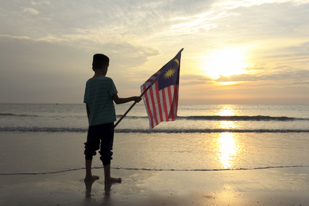The Concept of Independence Day - a boy holding the Malaysian flag on the shore at sunriseの写真素材