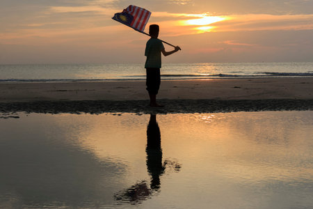 The Concept of Independence Day - a boy holding the Malaysian flag on the shore at sunrise
