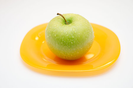 Green apple with drops of water on a yellow plateの写真素材