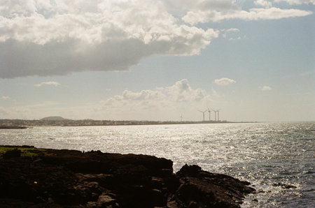 Sparkling ocean seascape with volcanic rocks in the foreground and distant wind turbines on the...