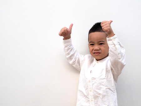 very happy asian boy making thumbs up sign and smiling happily on white background with paper spaceの写真素材