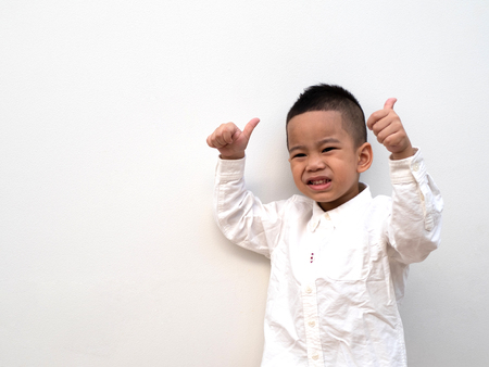 very happy asian boy making thumbs up sign and smiling happily on white background with paper spaceの写真素材