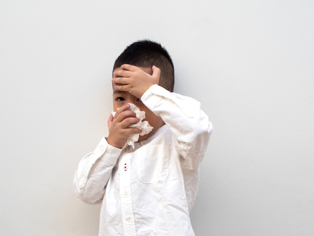 sick asian boy blow his nose into tissue on white background and paper spaceの写真素材