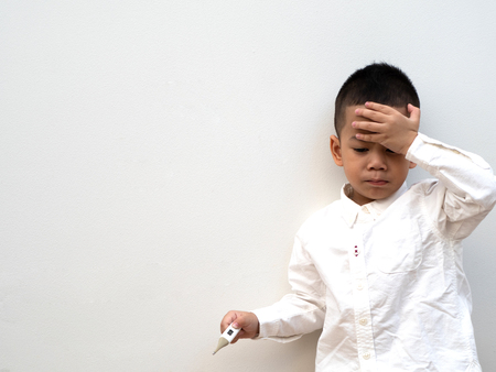 sick asian boy with thermometer in hand on white background and paper spaceの写真素材