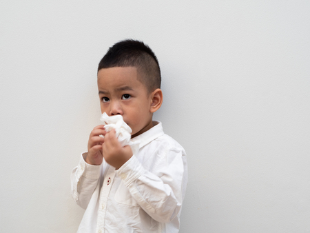 sick asian boy blow his nose into tissue on white background and paper spaceの写真素材