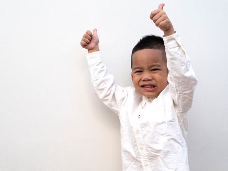 very happy asian boy making thumbs up sign and smiling happily on white background with paper spaceの写真素材