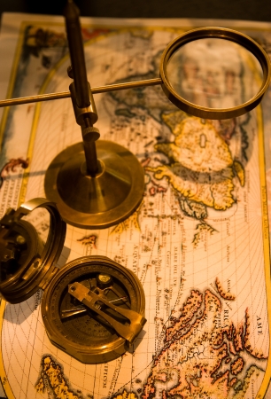 An old brass compass and magnifier on old world background の写真素材