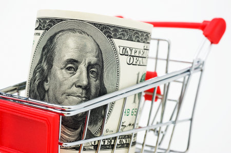 Shopping cart and stocks of dollars close up shot.