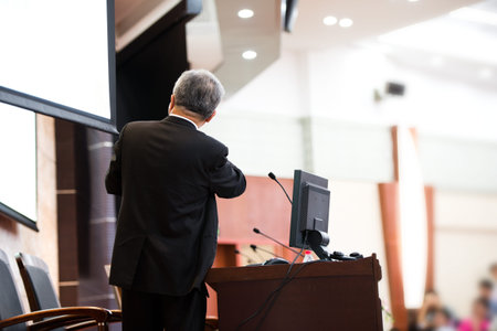Business man is making a speech in front of a big audience at a conference hall.
