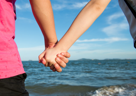 Summer couple holding hands in front of the sea.の写真素材