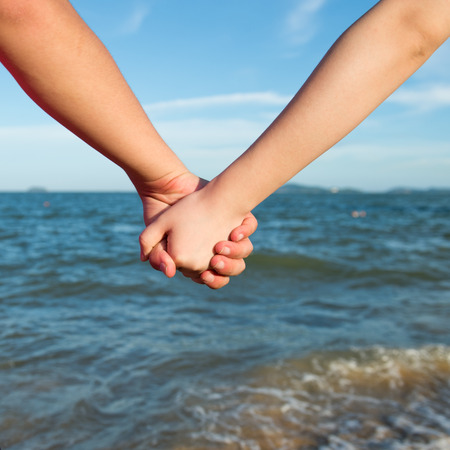 Summer couple holding hands in front of the sea.の写真素材